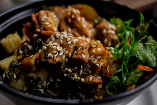 Glazed teriyaki chicken over rice in a black ceramic bowl with sesame seeds